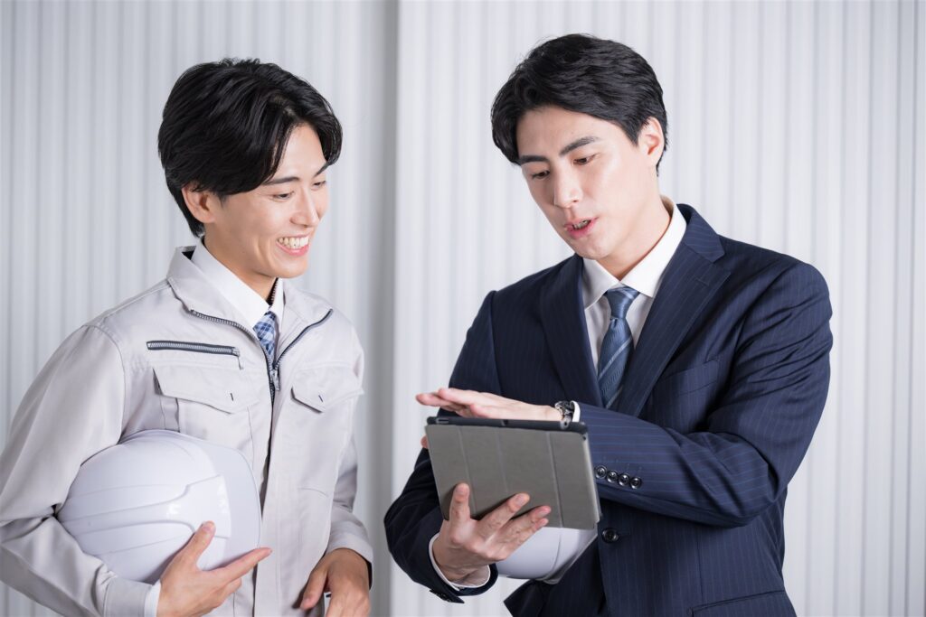 ヘルメットを抱えた作業服の男性とタブレットを持つ男性