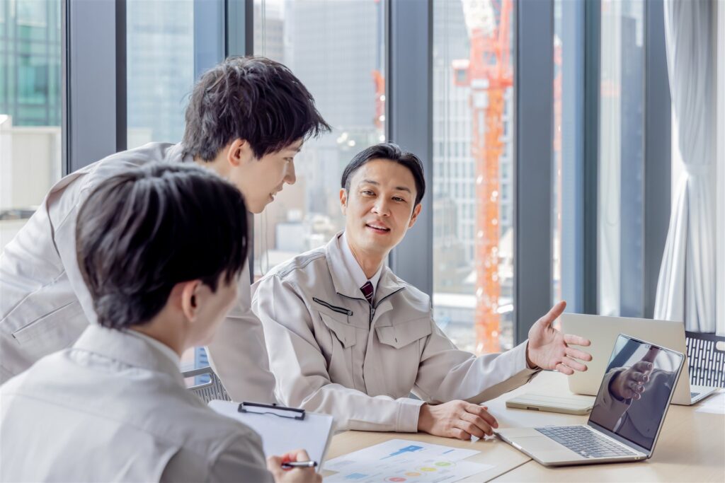 クレーンの見える会議室で話す作業服の3人