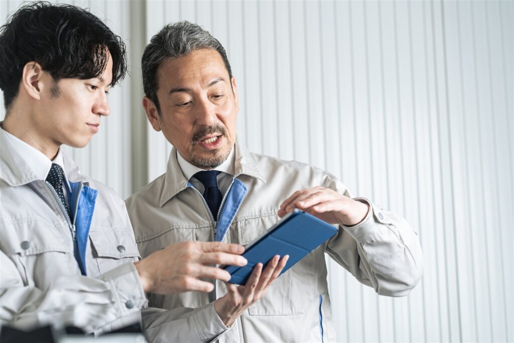 タブレットを見て話す作業服の若手と年配の男性