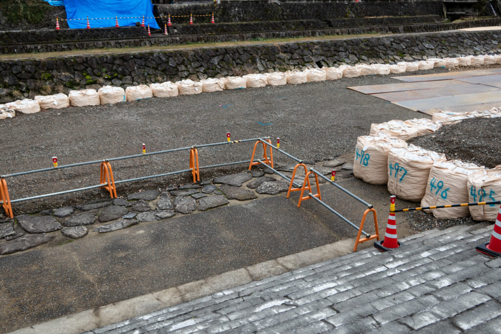 土のうと柵とカラーコーンが並ぶ河川敷の工事現場