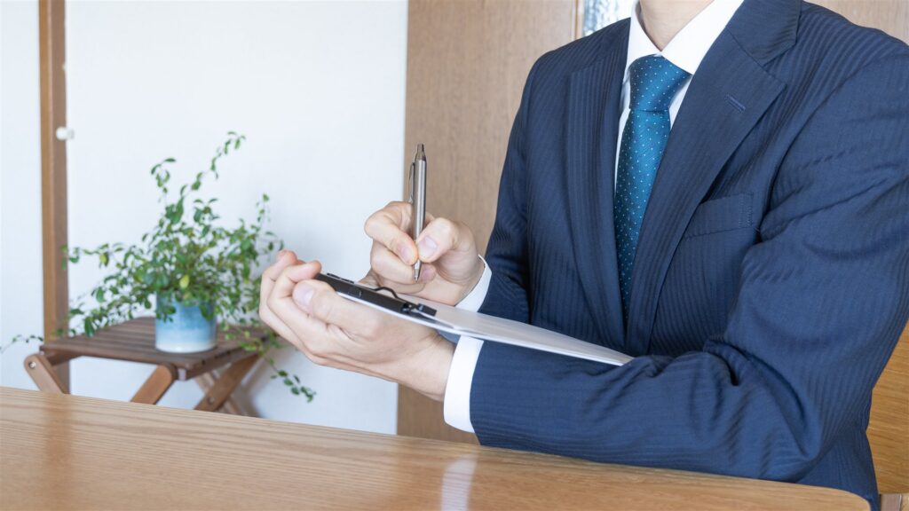 バインダーに書き込むスーツの人の手元