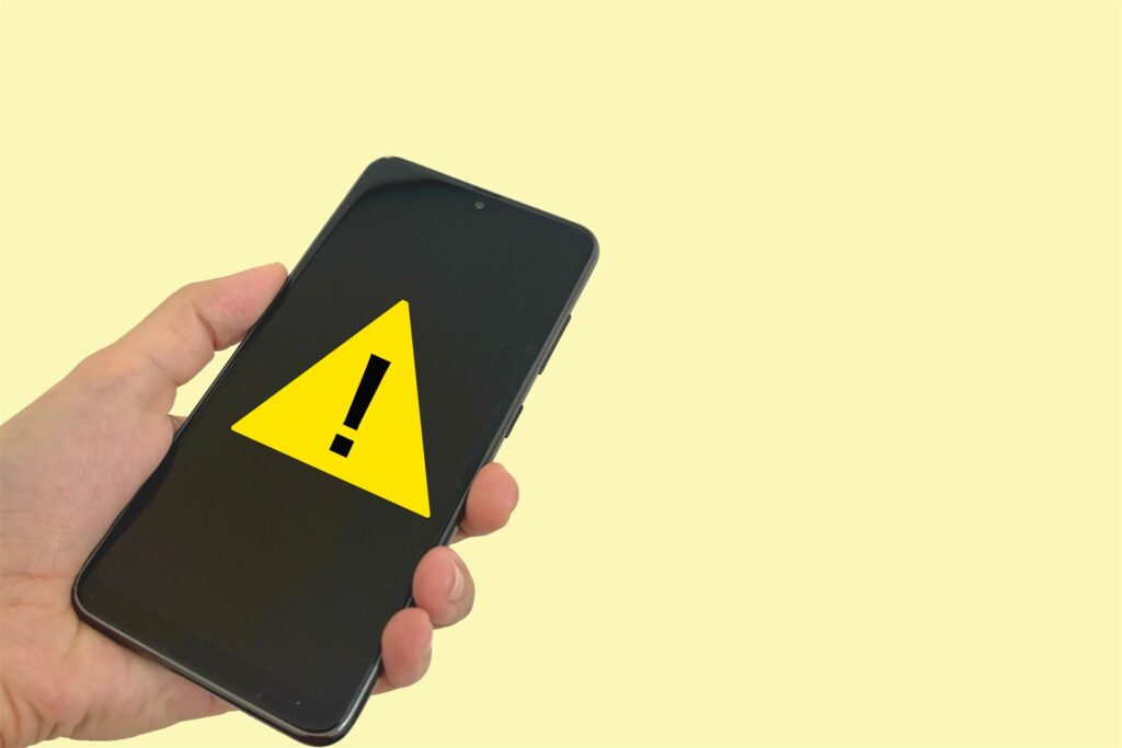 警告の印を出したスマートフォンを持つ手