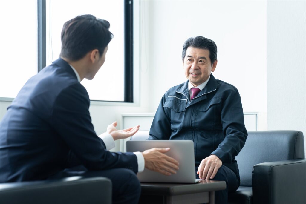 ノートパソコンを前に話し合う背広の男性と作業着の年配の男性