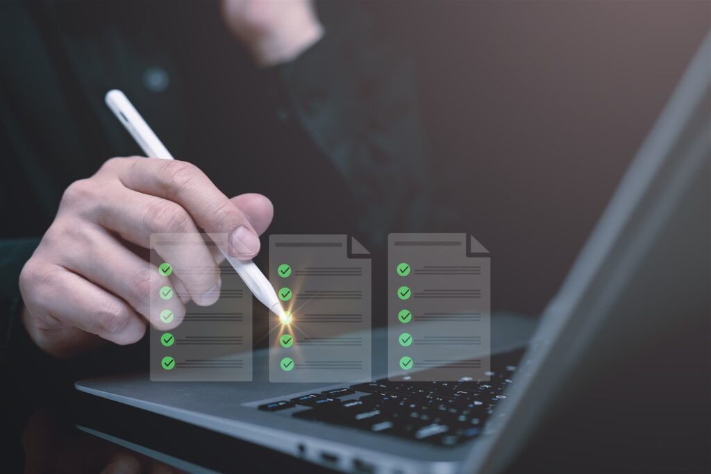 ノートパソコンの前でチェック欄の書類を確かめる手元