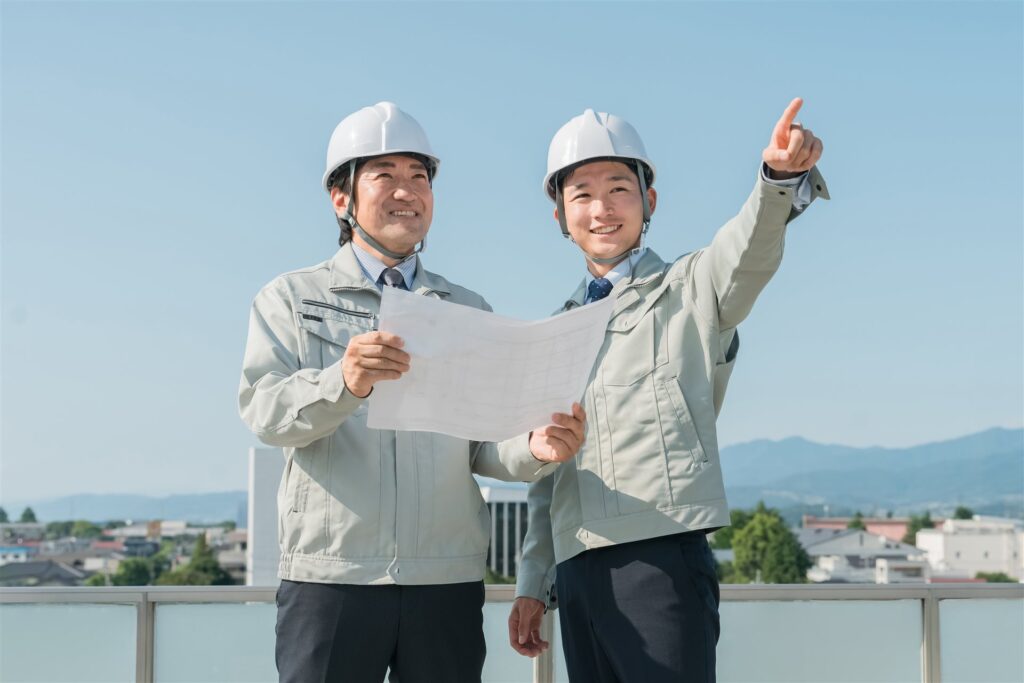 図面を手に遠くを指さすヘルメットの2人