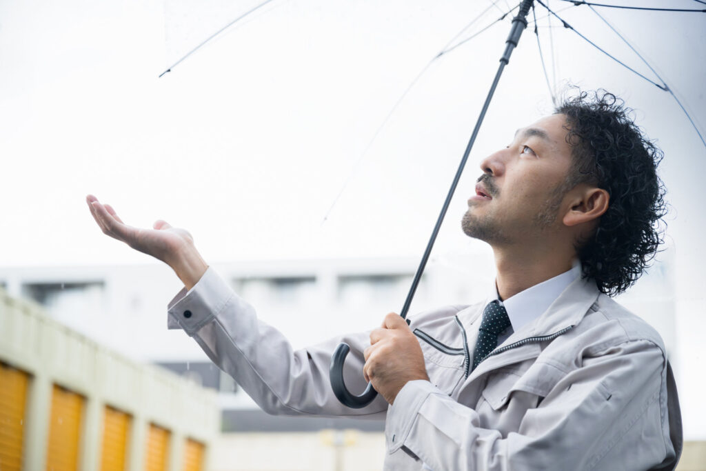 傘をさして手のひらで雨を確かめる作業着の男性