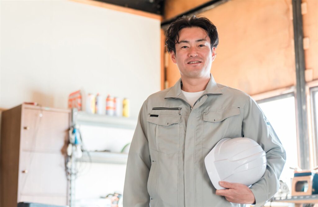 作業場でヘルメットを持つ作業着の男性