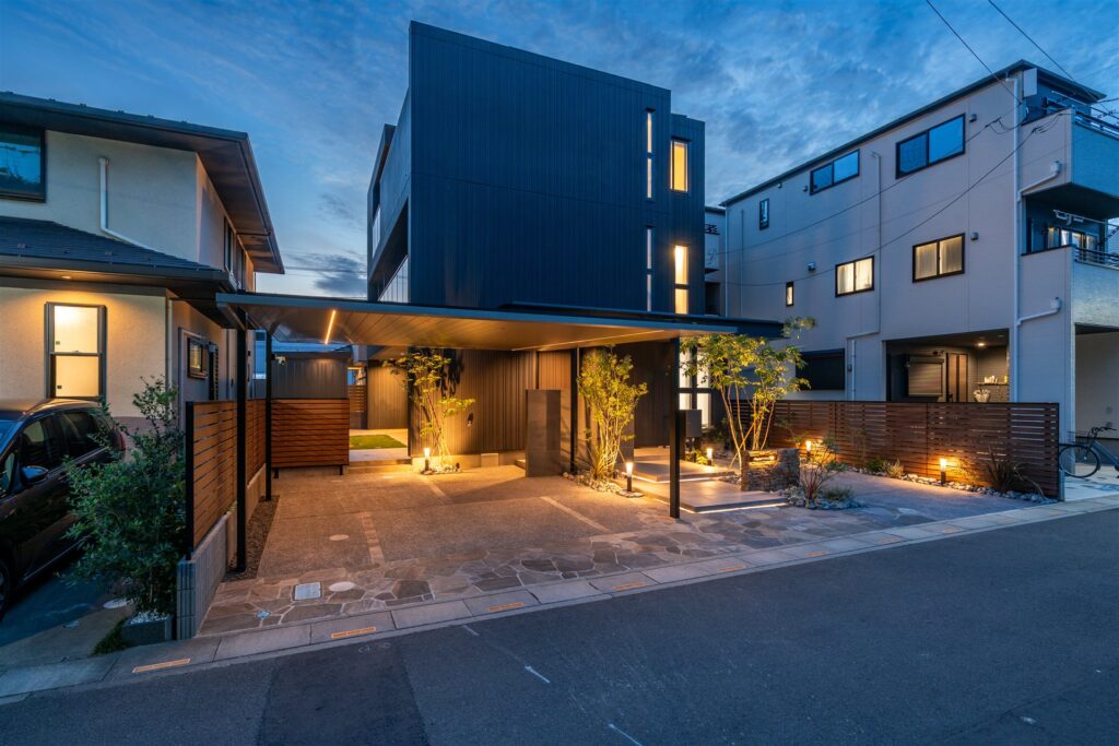 夕方の3階建て住宅の前の屋根つき駐車場と照明の植栽