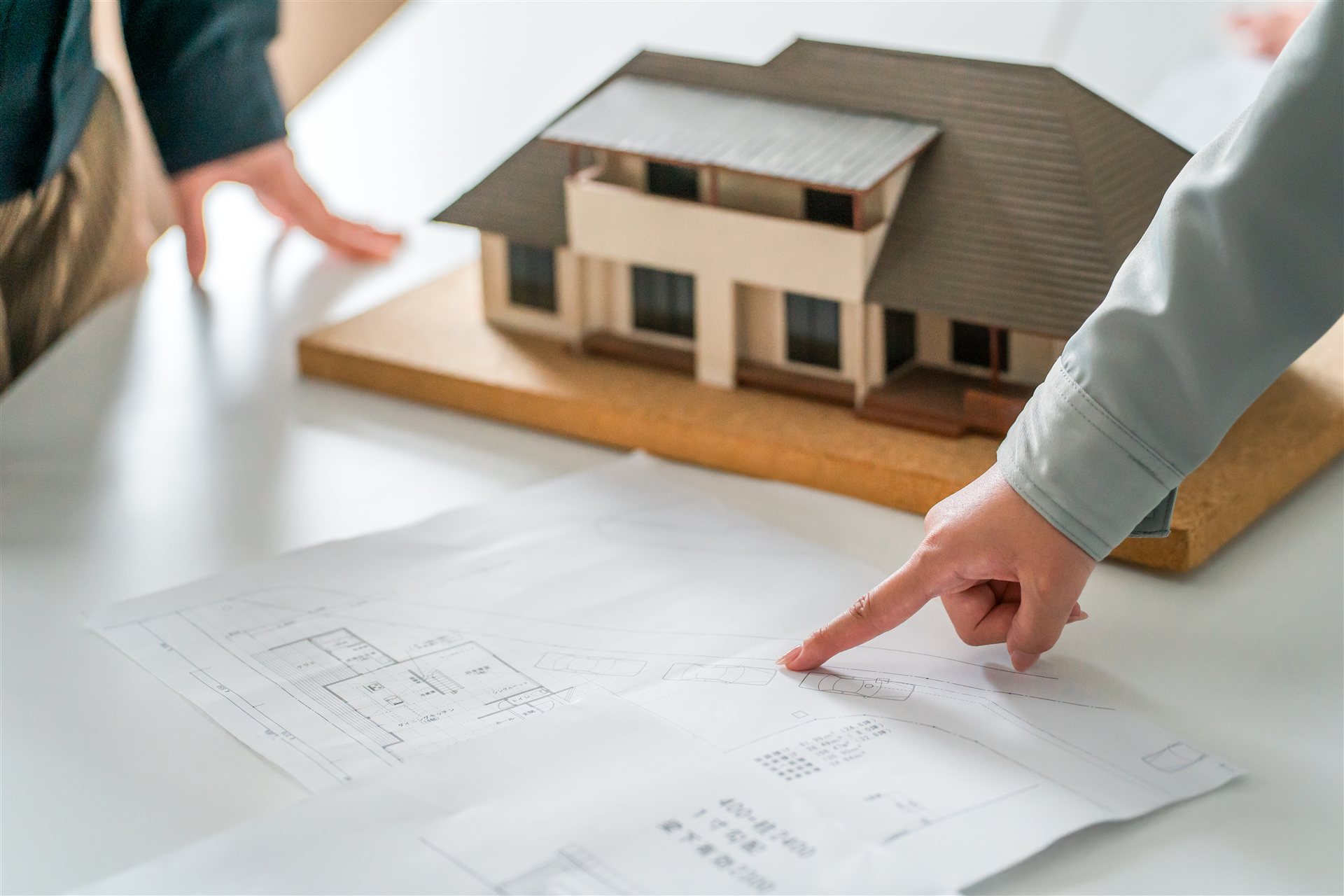 住宅の模型と設計図を指す手元