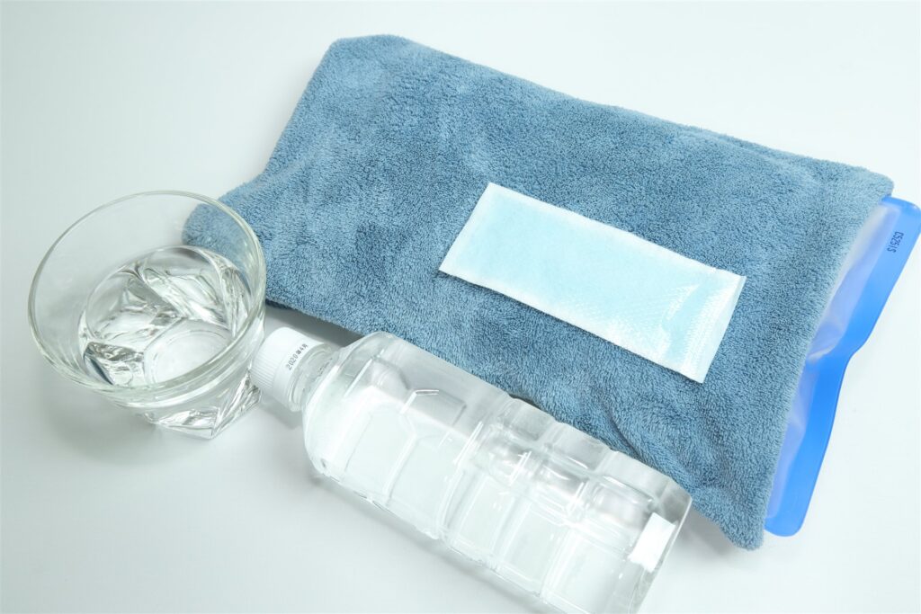 タオルで包んだ保冷剤と冷却シートと水のボトルとグラス