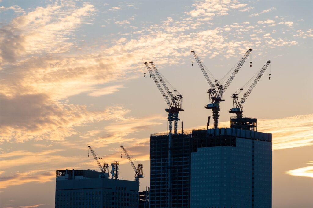 夕暮れの空にクレーンが並ぶ建設現場