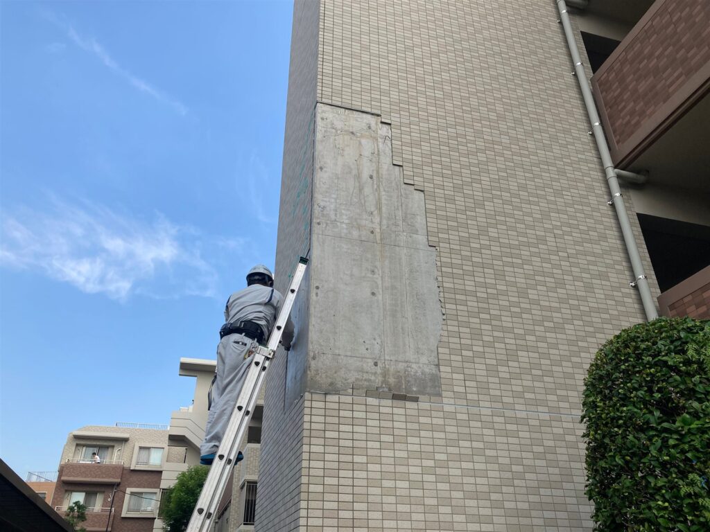 はしごに乗って外壁のタイルを直す職人
