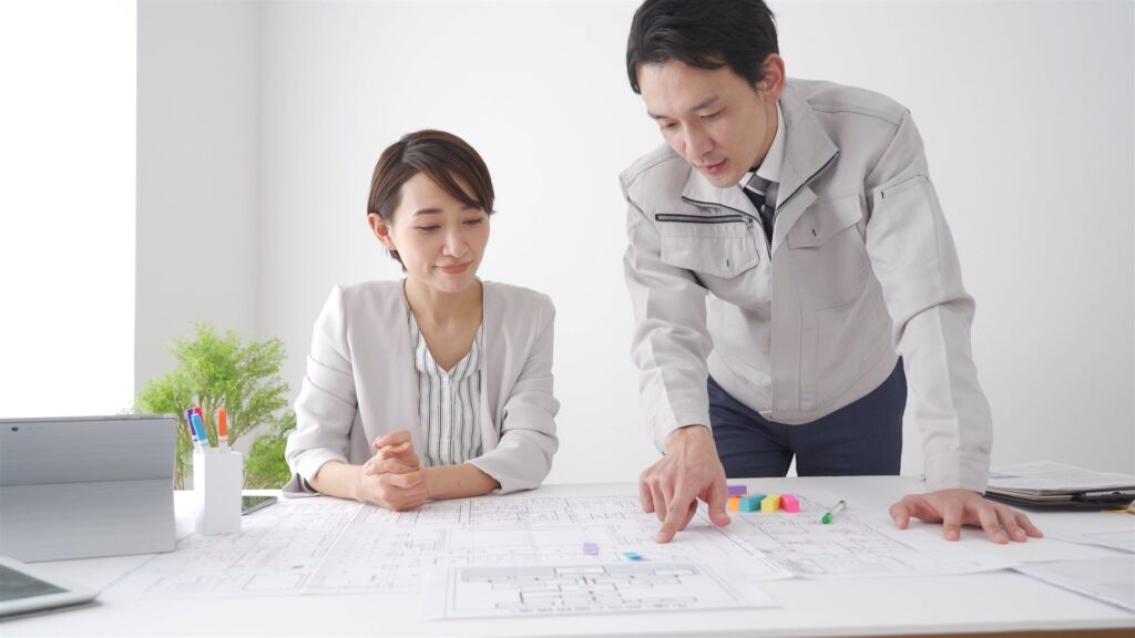 図面を広げて打ち合わせる作業着の男性と女性