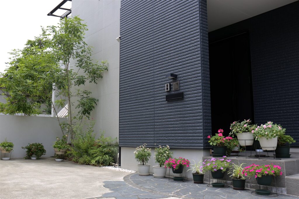 石張りのアプローチと鉢植えの花が並ぶ住宅の玄関前