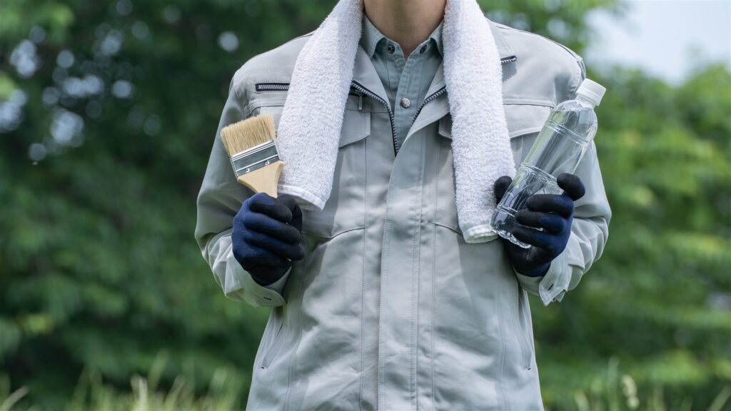 首にタオルを掛け刷毛と水のボトルを持つ作業服の人