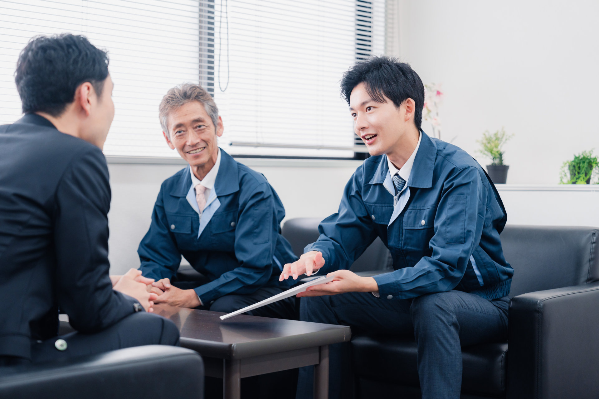 事務所で作業服の2人とスーツの男性が相談する