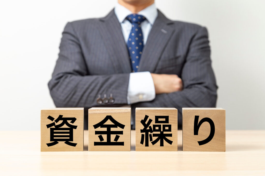 「資金繰り」と書いた積み木と腕を組む背広の人