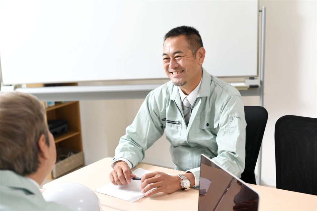事務所の机で向かい合って話す作業服の男性