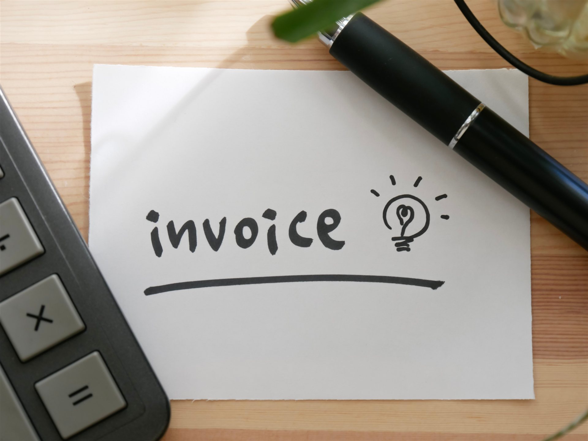 「invoice」と書いた紙と電卓とペン