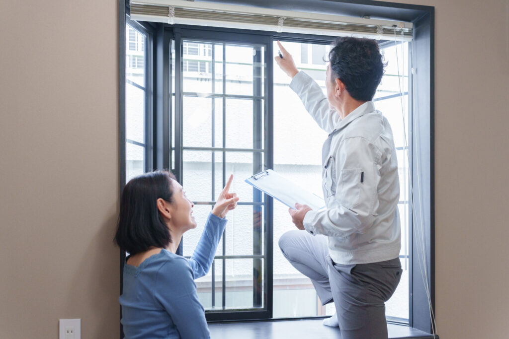 住宅の窓のサッシを職人が点検し住まいの人と話す