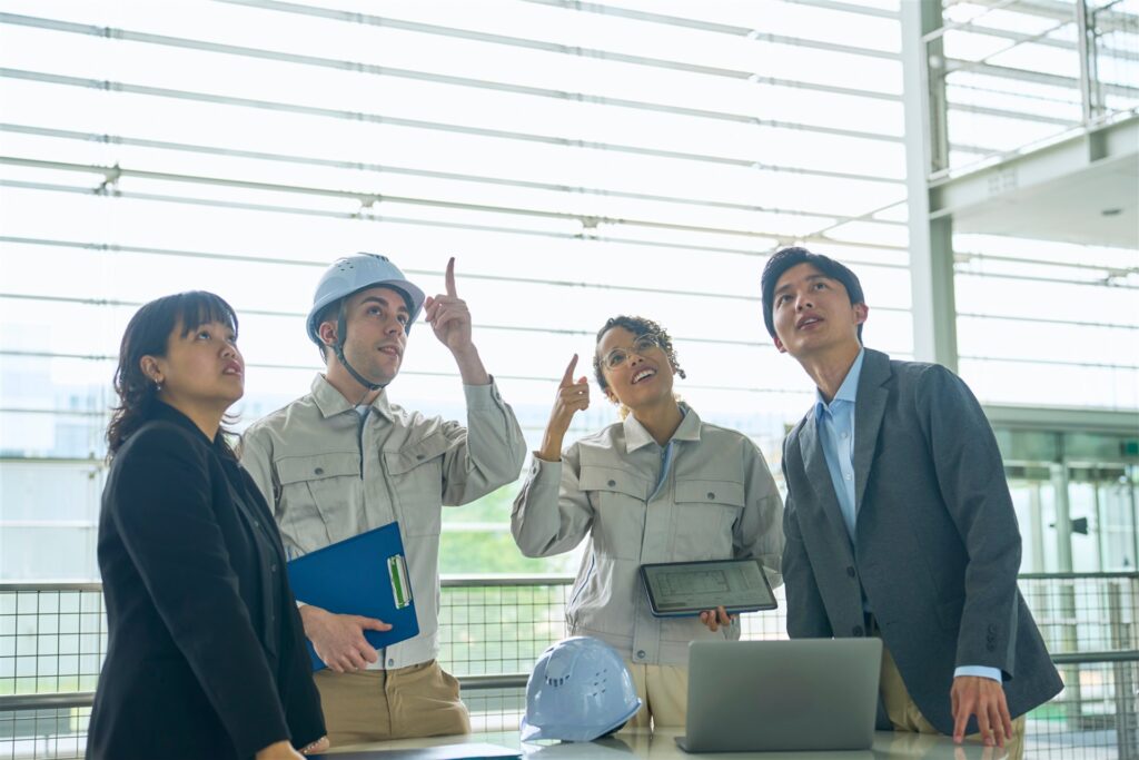 上を指して話す作業着と背広の4人
