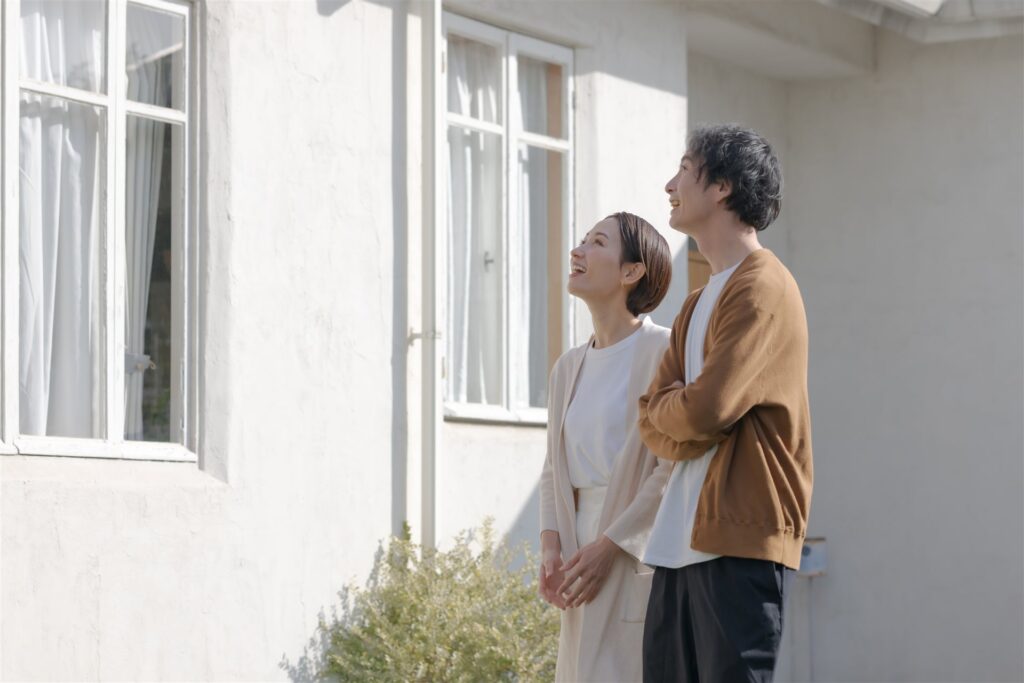 白い外壁の住宅の前で家を見上げる夫婦