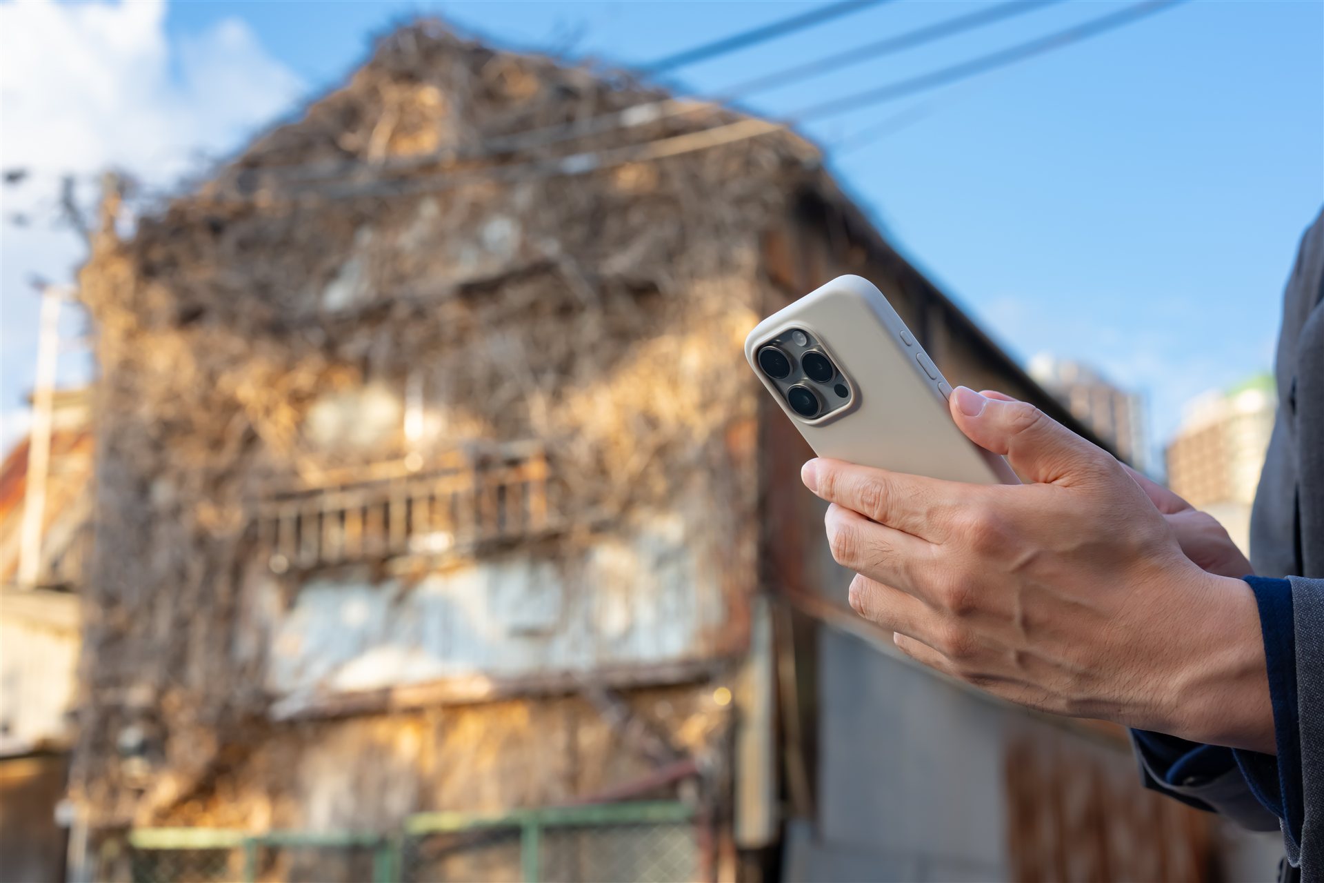 つたの絡んだ古い家の前でスマートフォンを構える手