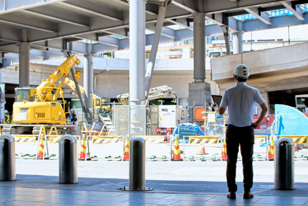 コーンと柵で囲った高架下の工事現場を見る人