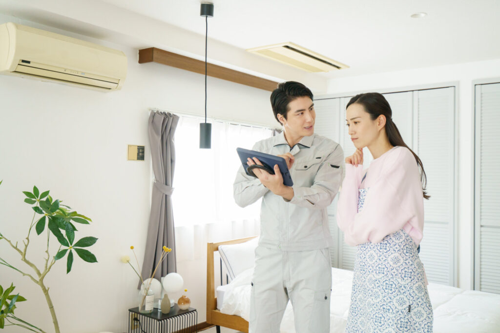 寝室でタブレットを見せる作業着の男性と話を聞く女性