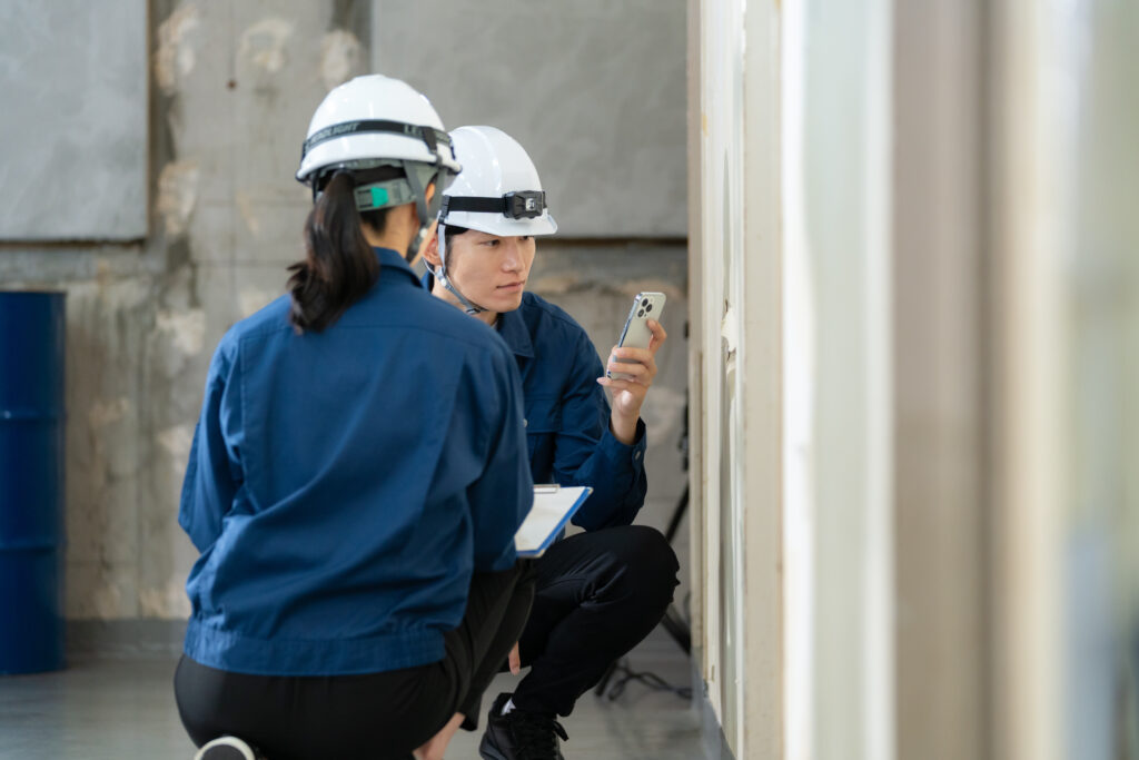 ヘルメットの2人がスマホで壁の傷みを撮って確かめる