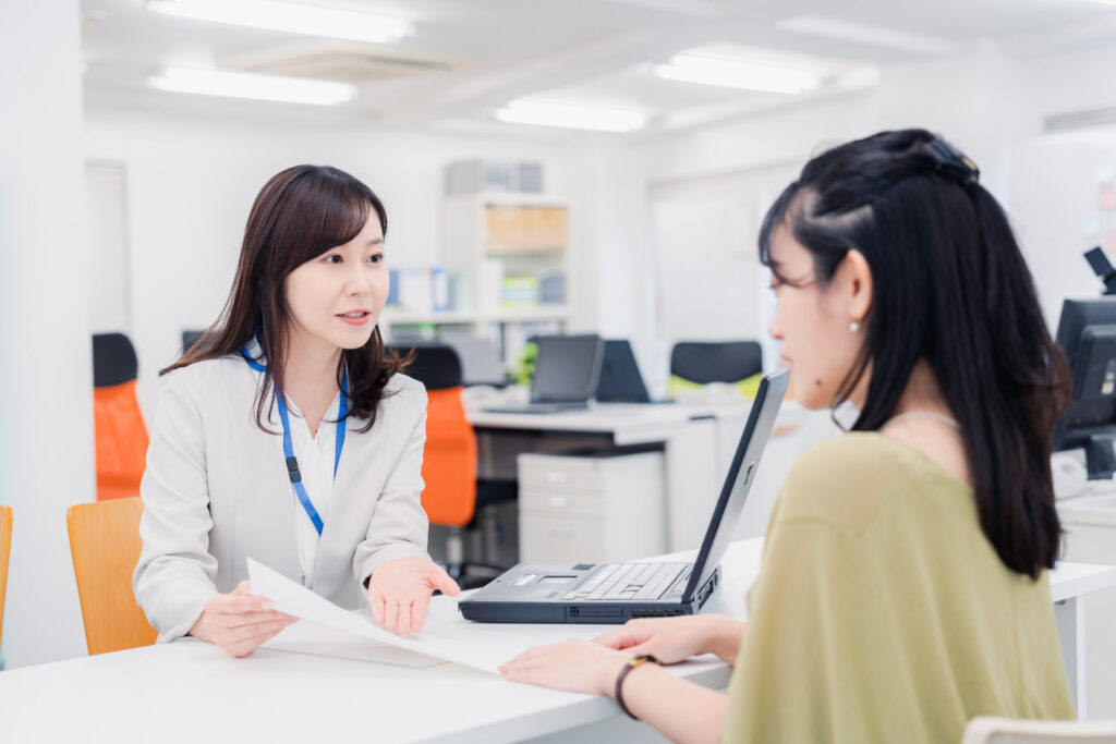 窓口で名札の職員が来た人に書類を示して説明する