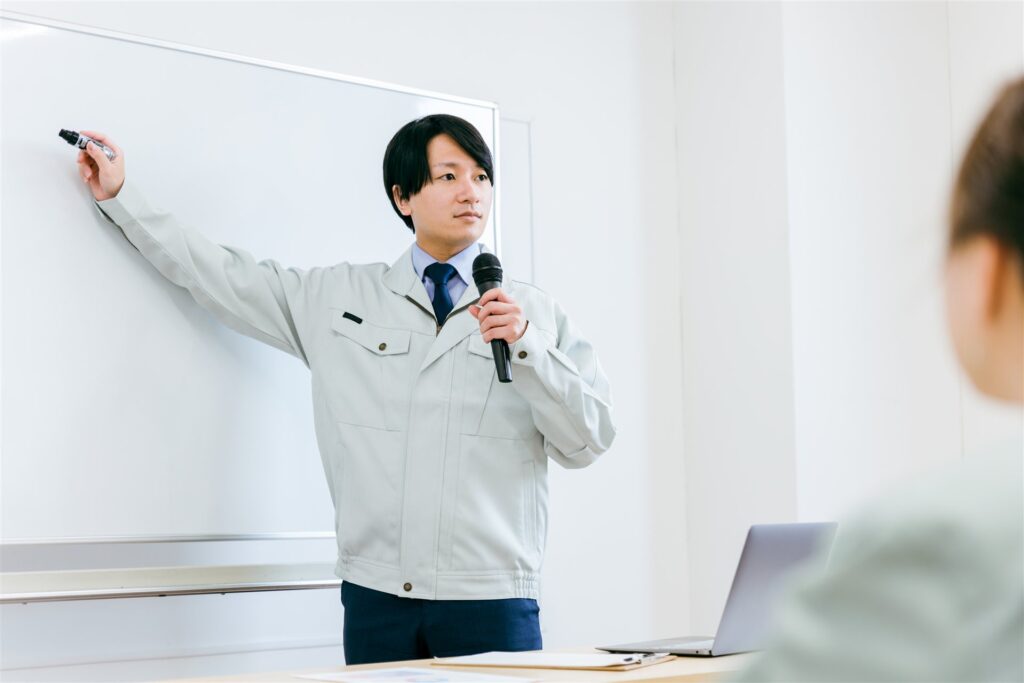 作業着の講師がホワイトボードの前で講習する