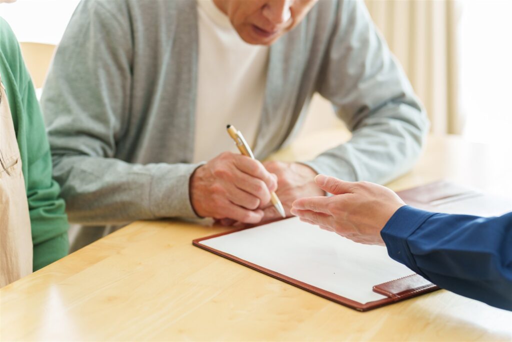 白い紙にペンで書き込むシニアの男性と説明する人の手
