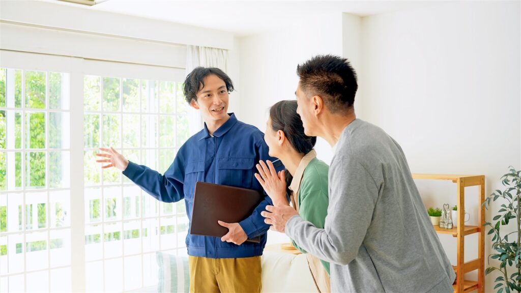 明るい部屋で作業服の担当者が年配の夫婦に部屋を案内する様子
