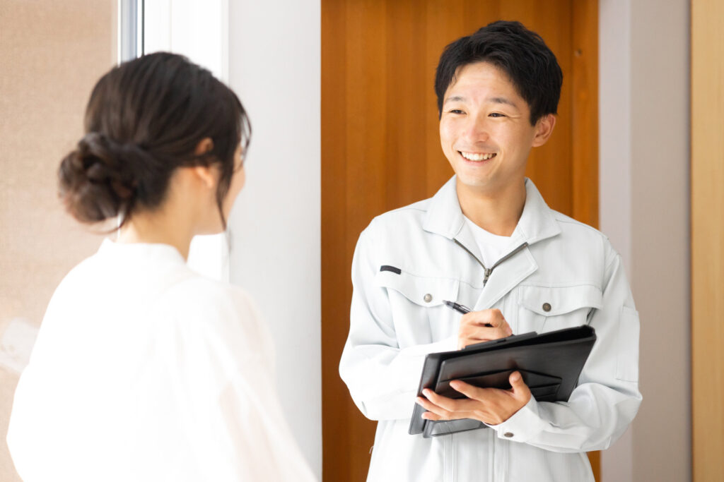 バインダーに書きながら女性と話す作業着の男性