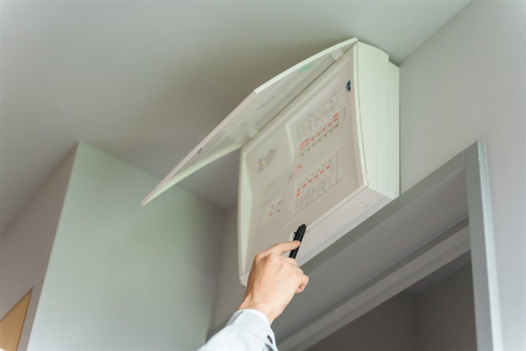 ふたの開いた分電盤をペンで指して確かめる手元