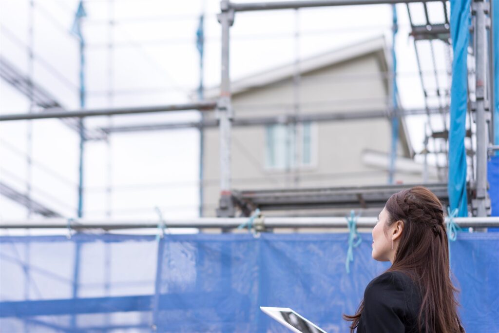 足場とシートで囲った住宅の工事現場とタブレットを持つ人