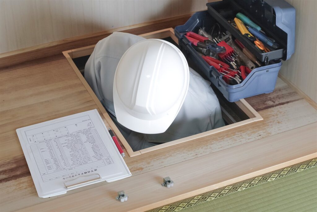 床下の点検口から床下を調べる作業員と点検表