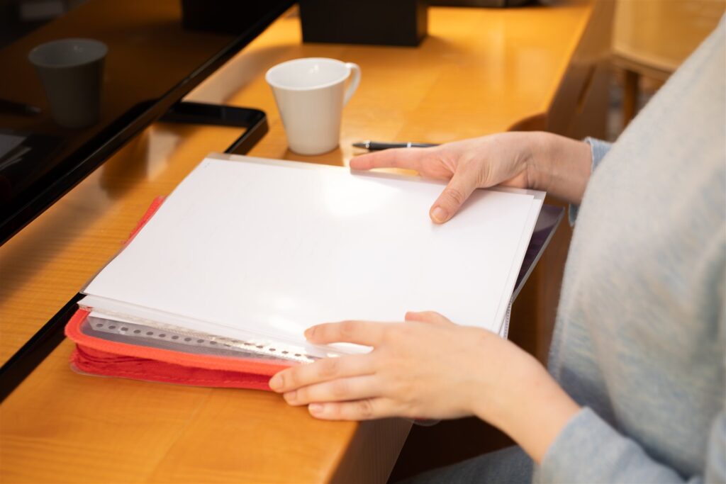 赤いファイルの書類をそろえる手元