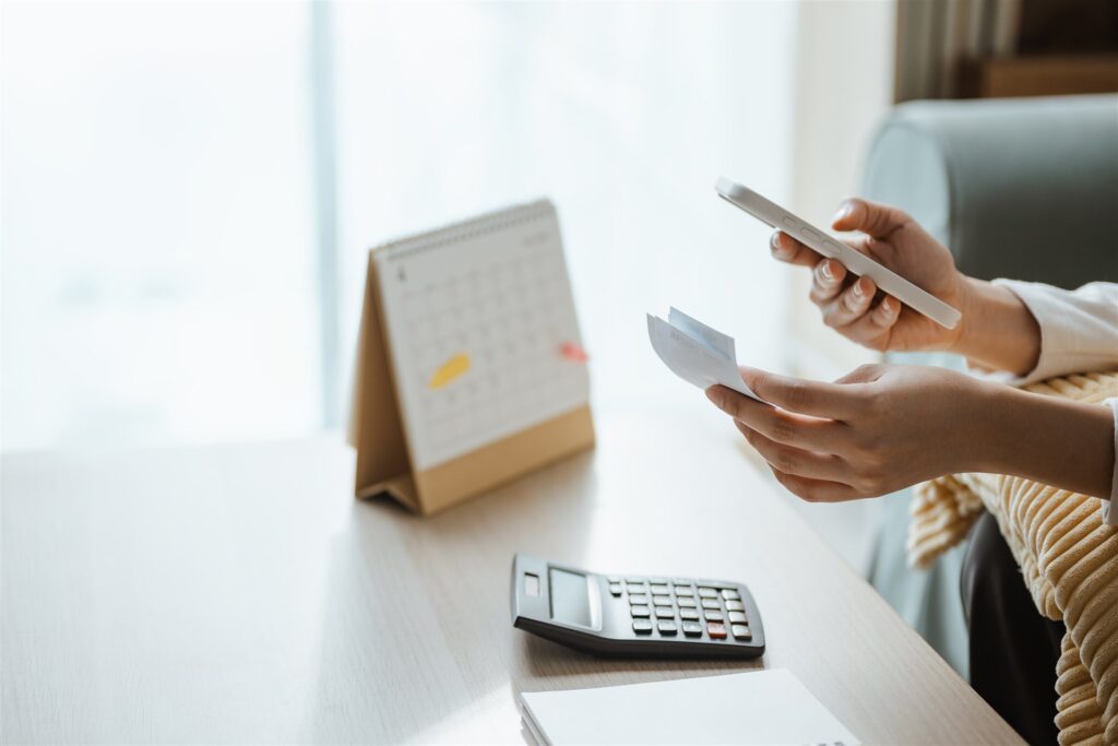 レシートとスマホを手に電卓のある机に向かう手元