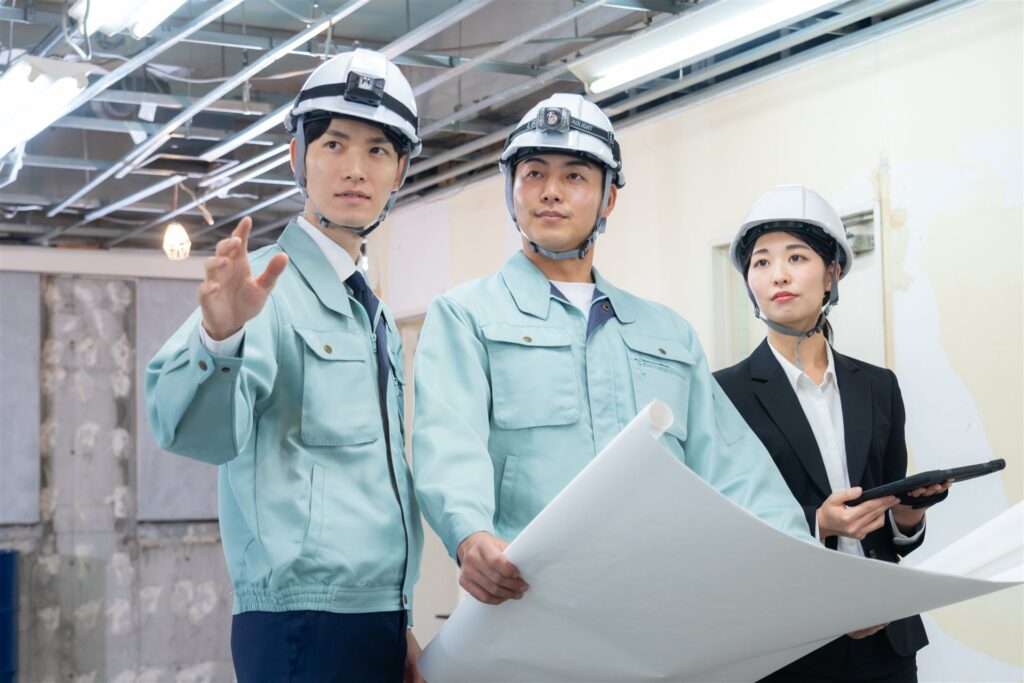 図面を持って話す作業着の3人