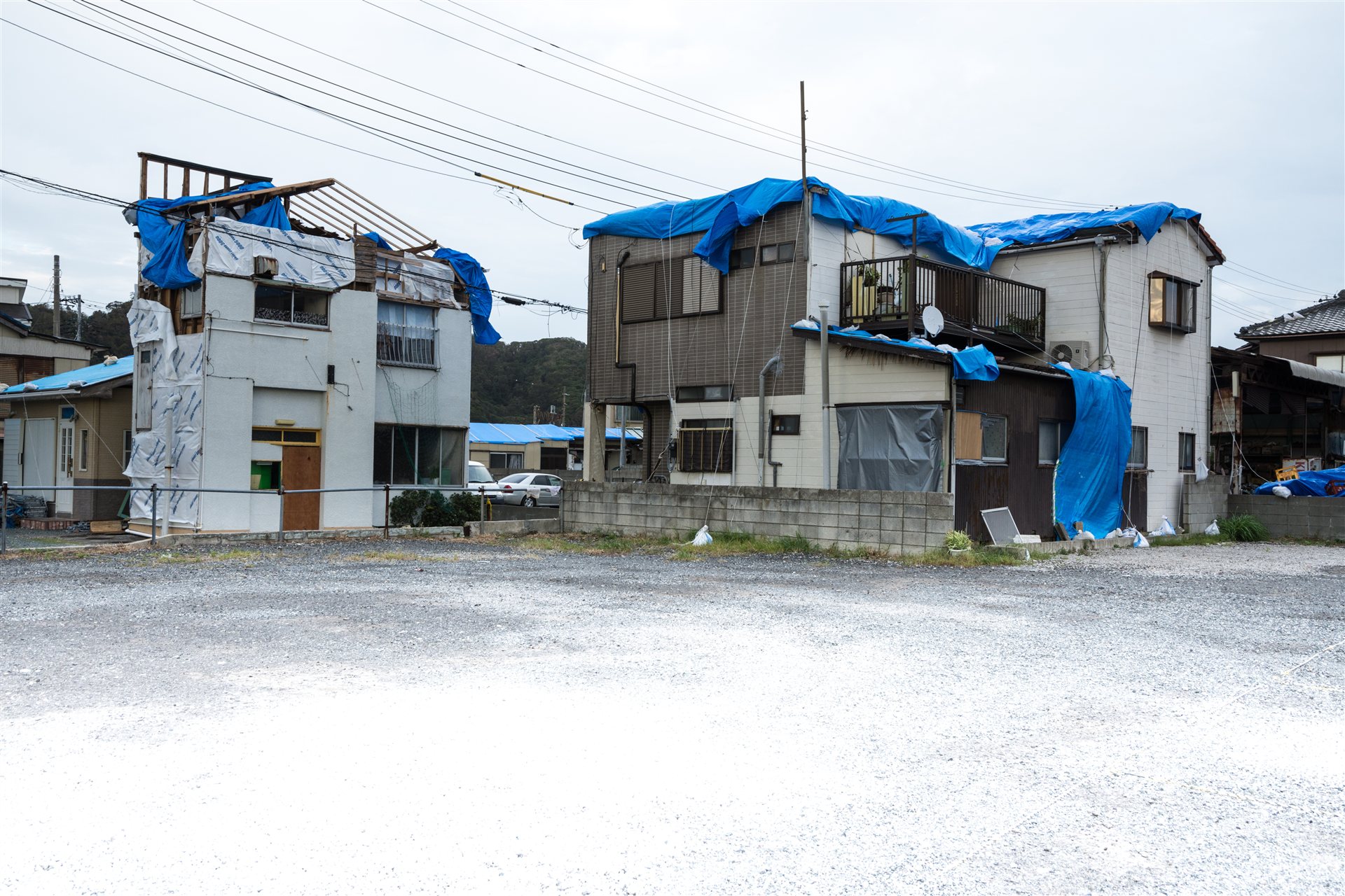 屋根と外壁にブルーシートを掛けた2階建ての住宅