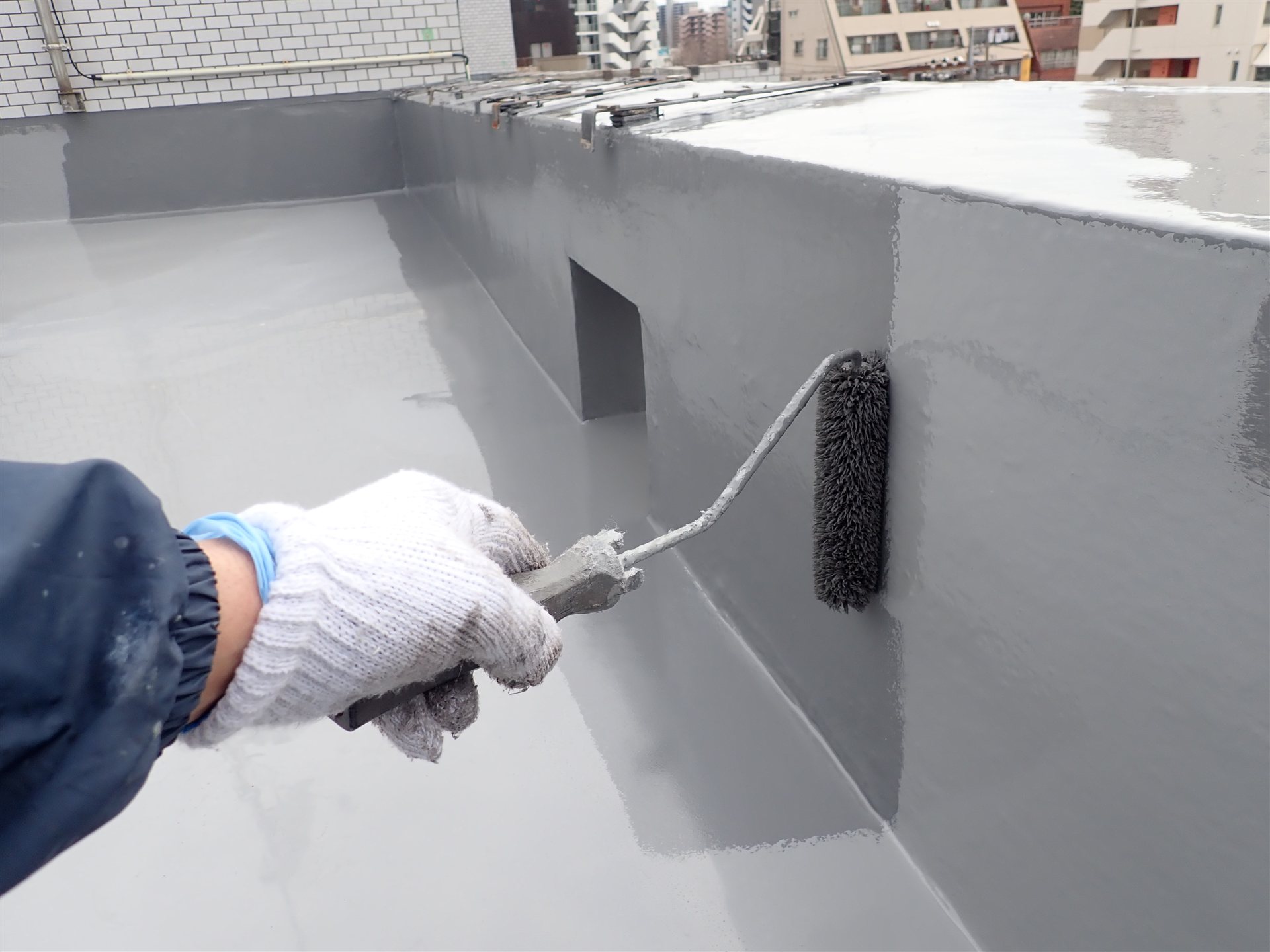 屋上の立ち上がりに防水材をローラーで塗る手元