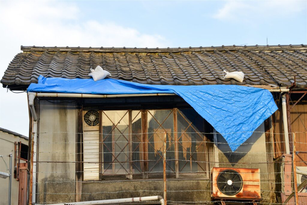 ブルーシートで覆った古い家の瓦屋根