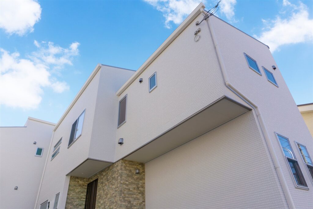 青空の下の白い外壁の2階建ての住宅を見上げた様子