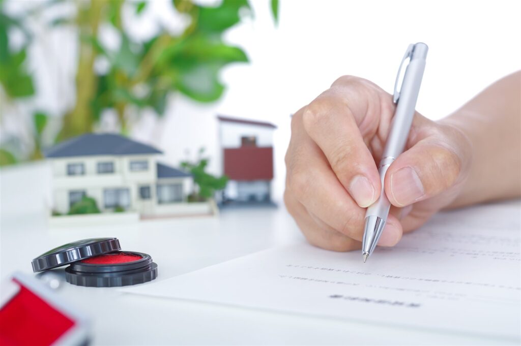 住宅の模型の横で書類に署名する手元