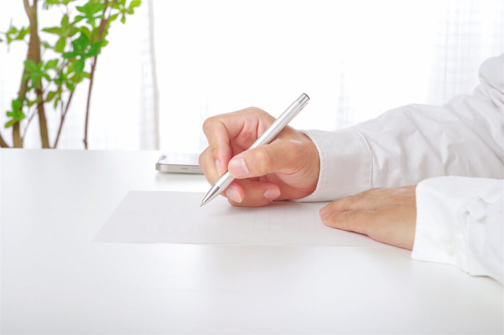 白い机で用紙にペンで書く手元