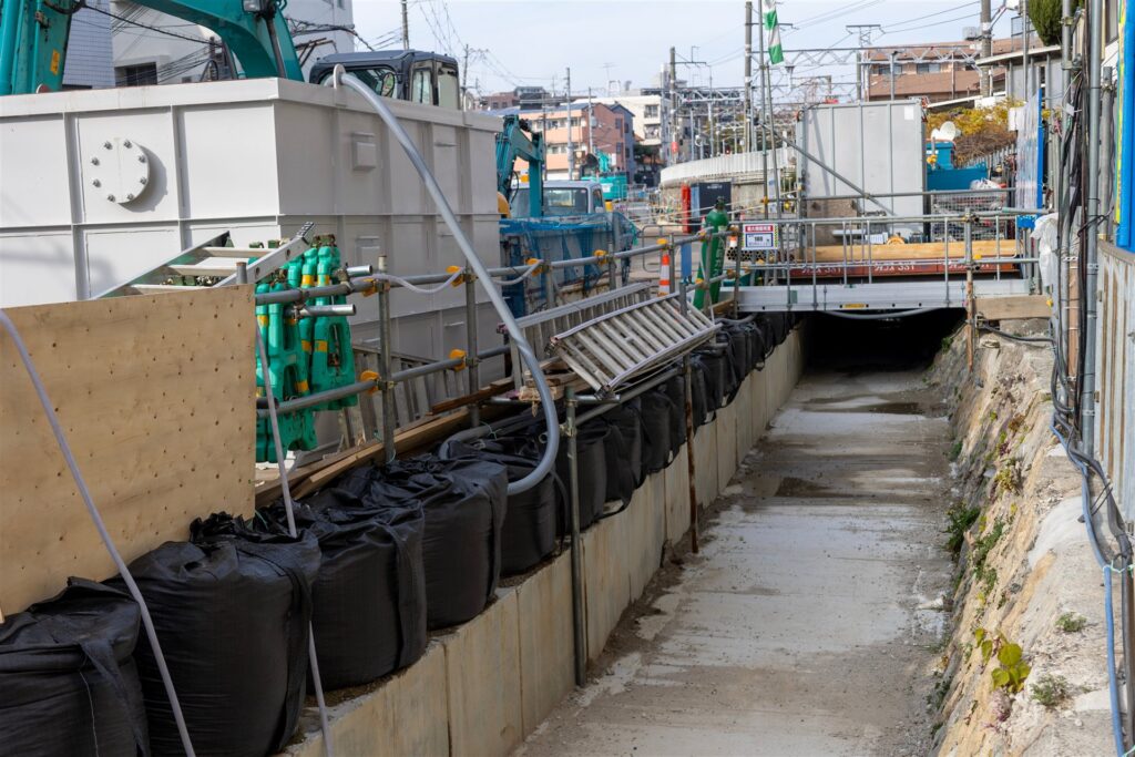 コンクリートの水路に沿って並ぶ黒い土のうと仮設の手すり