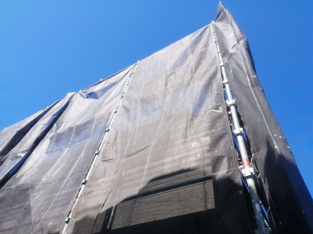黒い養生シートで覆われた建物を見上げた様子